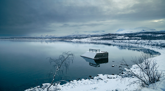 Panoramic view of Torneträsk lake with snowy mountain under a dark cloudy sky in winter in the Abisko National Park