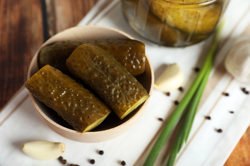 Bowl with tasty pickled cucumbers and ingredients on wooden table, closeup