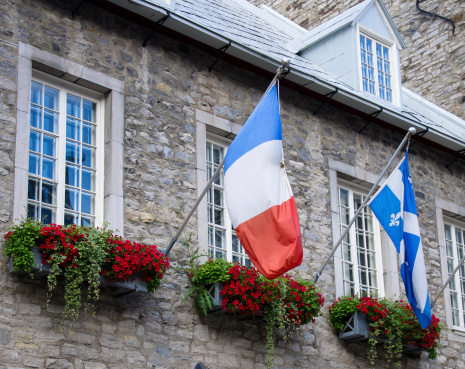 Charming window with the flags of France and Quebec in contrast to the stone wall of the building.