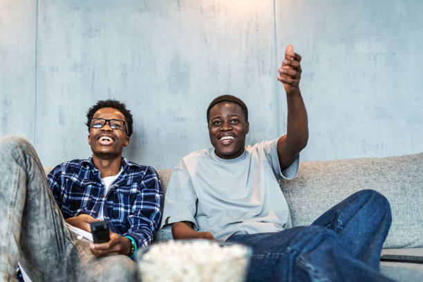 Two male black friends watching sport game on TV with popcorn stock photo