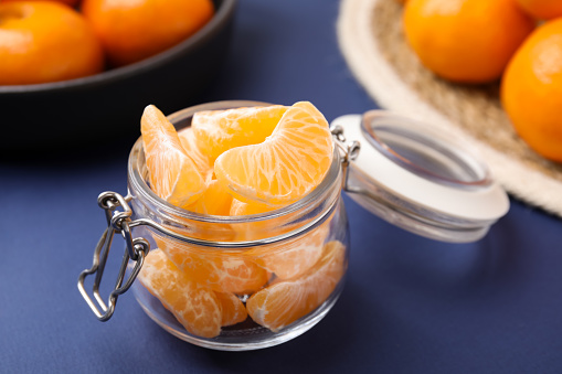 Glass jar of fresh juicy tangerine segments on blue table, space for text