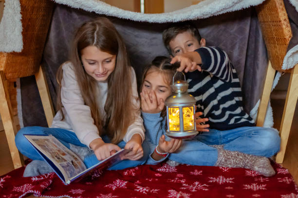 istock Three Little Children With Flashlights Reading Scary Stories In A Tent At Home. 1797274441
