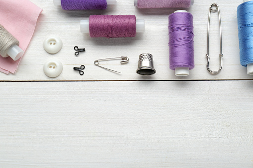 Flat lay composition with thimble and different sewing tools on white wooden table. Space for text