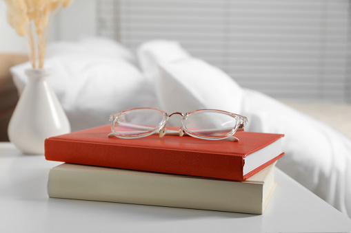 Books and glasses on white wooden bedside table in bedroom