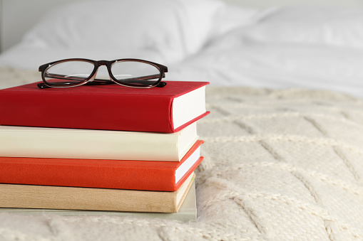 Books and glasses on white soft blanket in bedroom, space for text