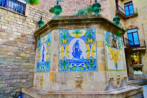 Barcelona, Spain: 10/31/2023- El Font de Santa Ana dates back to 1356 and is the oldest fountain in Barcelona. The hexagonal stone structure has decorative blue, while and green tile. The drinking water comes from two brass taps.