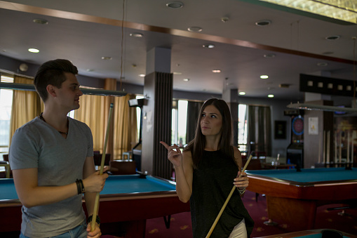 Group of friends playing billiards and smiling in night club. Focus on the billiard ball