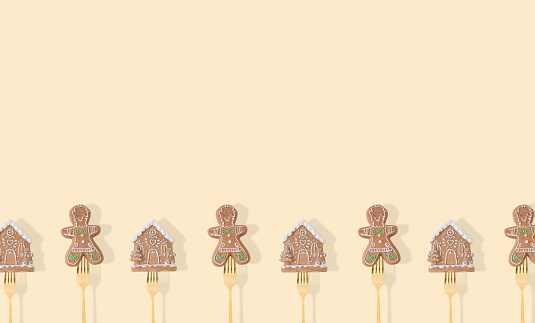 Gingerbread Christmas tree decorations pricked on a forks on pastel beige background. Minimal style New Year party background. Creative Christmas or New Year concept. Winter holidays idea. Copy space.