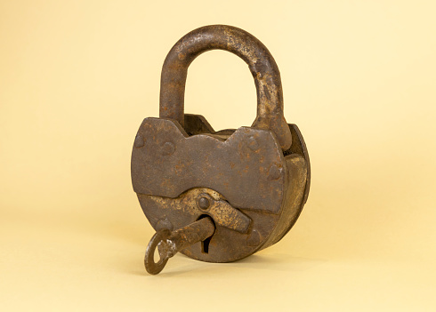 An old rusty padlock with a key in the middle on a beige background