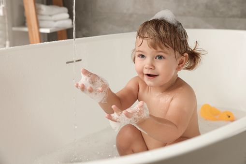Cute little girl taking bubble bath indoors. Space for text