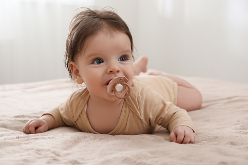 A 6 month old baby boy smiling with a pacifier in his mouth as he holds his little bare feet.