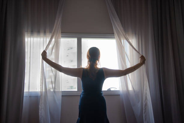 istock Woman in backlight opening curtain on bright day 1797447425