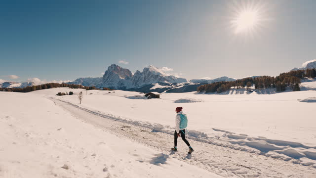SLO MO Young Female Backpacker Walking on Snow Covered Mountain Road Under Sunny Sky in Dolomites