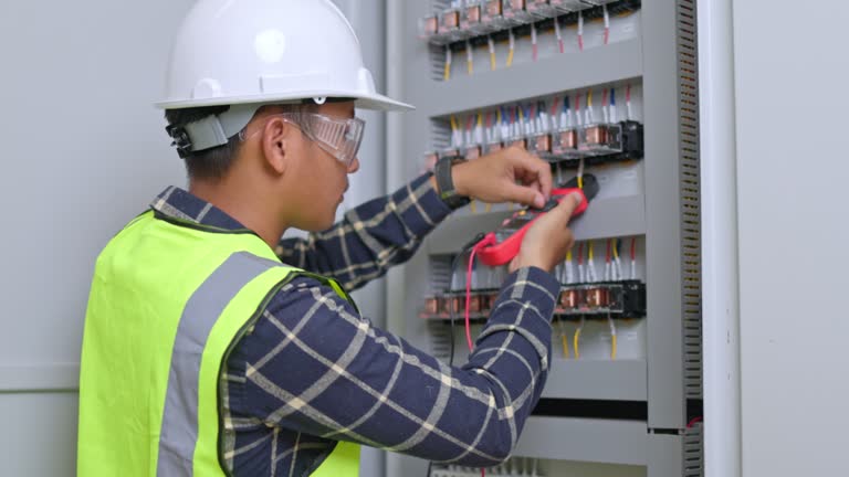 Electrician engineer work tester measuring voltage and current of power electric line in electical cabinet control. Electrician measurements with multimeter testing current electric in control panel.