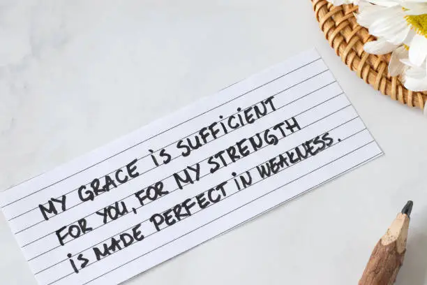 My grace is sufficient to you, for My strength is made perfect in weakness, handwritten Christian quote with flowers and pencil. Faith, trust, and peace in God Jesus Christ (2 Corinthians 12:9 verse).