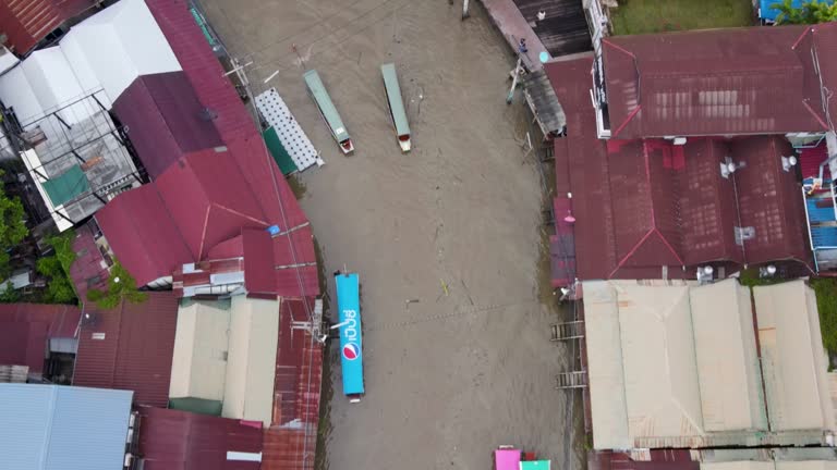 Boats travel down narrow, dirty canal past dilapidated buildings. Aerial top down, dolly forward