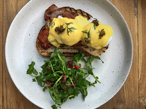 Close-up shot of bacon eggs benedict with hollandaise sauce on top of sourdough ,and watercress on the side