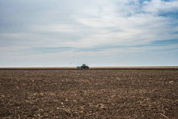 istock Tractor plows agri field, wind turbine on background. 1797586089