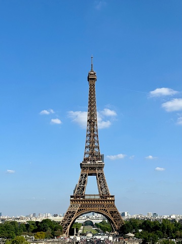 Eiffel Tower against the backdrop of the Champe de Mars park, city-line and blue sky