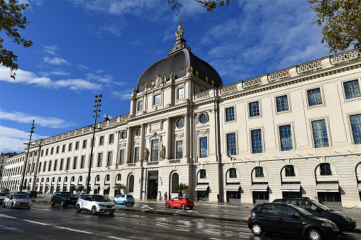 Lyon, France-11 04 2023: Cars passing in front of the facade building of the Lyon Grand Hotel-Dieu, a former hospital converted into a luxury Hotel, France.