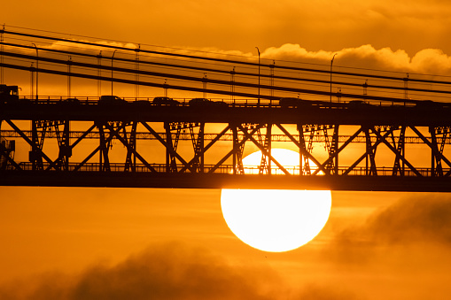 Car traffic on the bridge and a big bright sun setting down at orange sunset. Mid shot