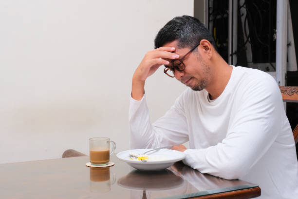 un homme assis à la table à manger regardant sa nourriture avec une expression paresseuse - pusing photos et images de collection