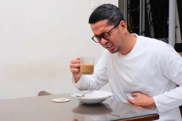 A man suffering stomach ache after drinking a cup of coffee