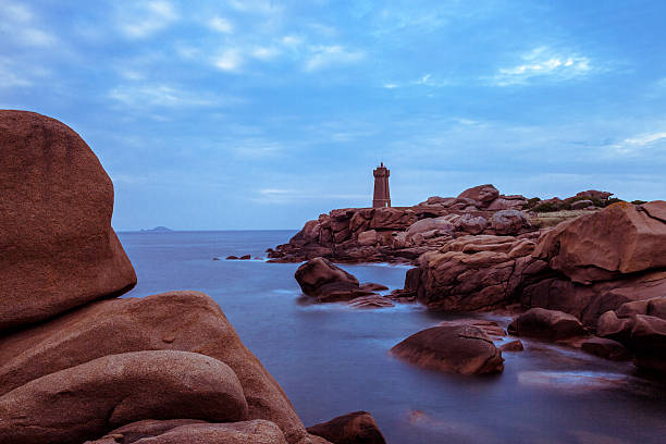 Cote D'armor in Brittany.  Horizontal long exposure of the Phare de Men Ruz and the rocky pink coast of Ploumanac'h in a cloudy summer sky