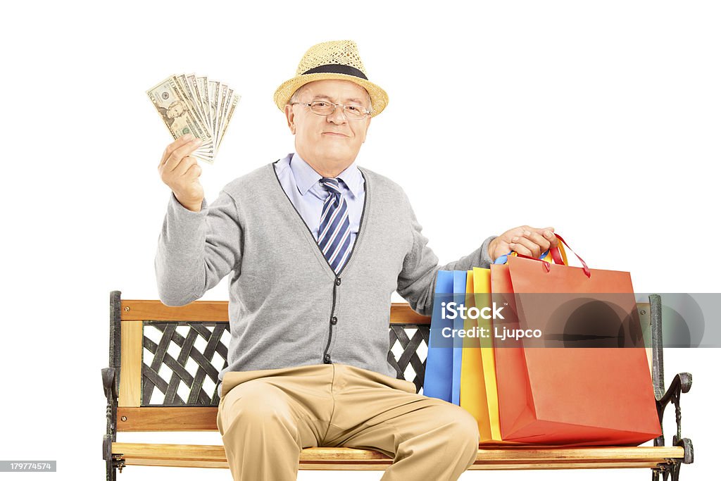 Uomo sorridente seduto su una panchina e holding dollari - Foto stock royalty-free di Abbigliamento