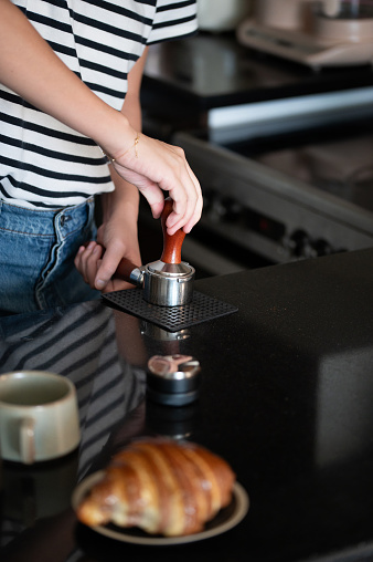 Female barista using a tamper to press freshly ground coffee into a portafilter