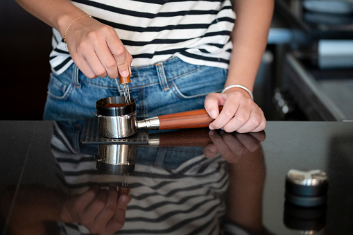 Female barista pushing coffee with distribution tool in a portafilter. Making espresso at home