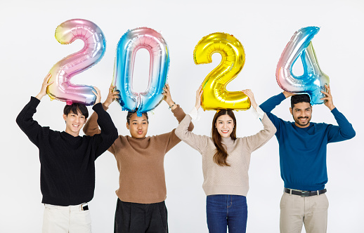 Isolated cutout full body studio shot group of Asian Indian happy cheerful male female friends wear colorful sweater standing smiling hold balloons number 2024 celebrated New Year on white background.