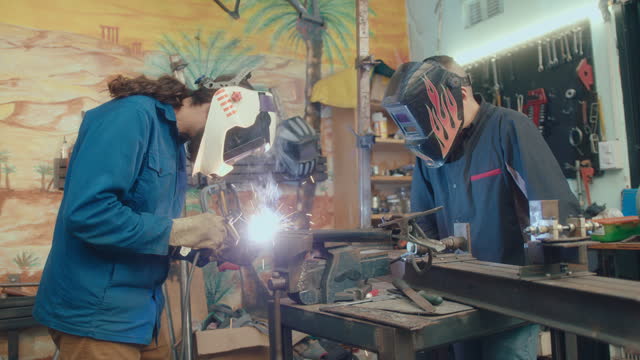 Two Coworkers Welding Metal Workpieces Together in Repair Shop