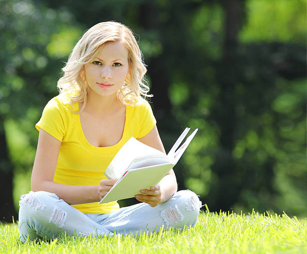 istock Girl reading book. Beautiful blonde sitting on grass. 179787639