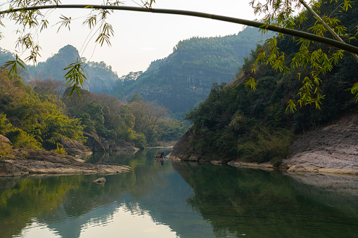 Peaceful evening landscape with the river, mountains and a boat in Wuyishan, Fujian, China. Bamboo on the foreground