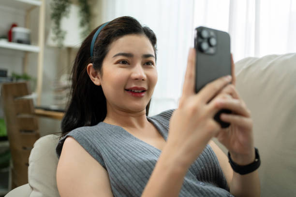 istock Smiling asian woman lying down on a cozy sofa using mobile banking pay financial bill via smart phone in living room at home 1797909939