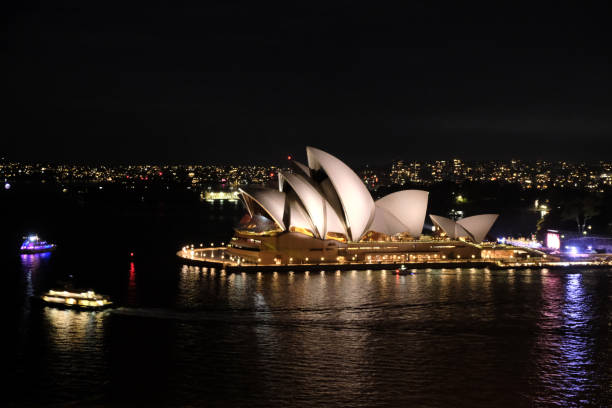 Sydney Australia - August 19, 2019: Night-time in Sydney, and the brightly-illuminated shape of the city's Opera House seems to glow in the darkness.