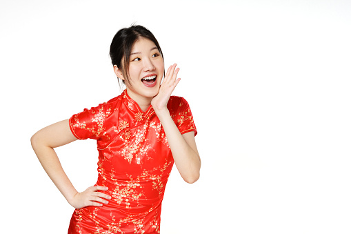 Asian woman wearing traditional cheongsam qipao dress with gesture shouting and holding palm near opened mouth isolated on white  background. Happy Chinese new year.