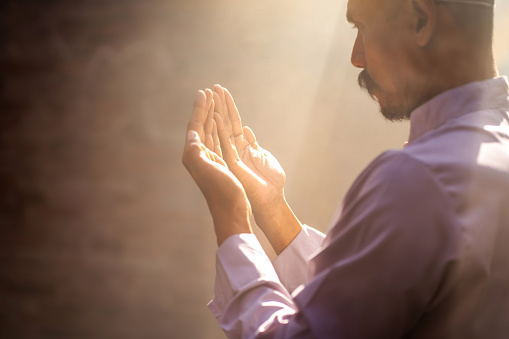 Silhouette of a Muslim man praying for blessings in a sunlit old Islamic mosque.
