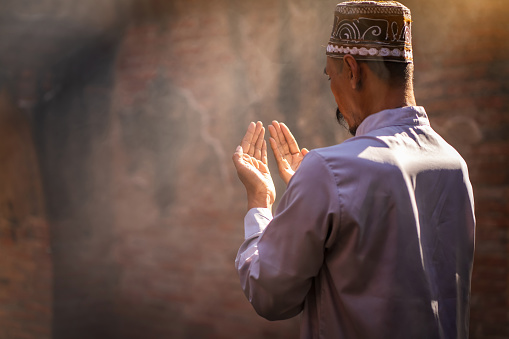 Silhouette of a Muslim man praying for blessings in a sunlit old Islamic mosque.