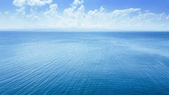 Aerial view of a blue sea water background and sun reflections. Aerial flying drone view. Waves water surface texture on sunny tropical ocean. Aerial photography.