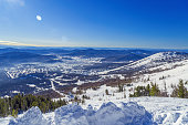 Winter nature panorama with Sheregesh ski resort in Altai, Russia, picturesque nature, sun flare on blue sky, white snow slopes and ski track, top view with range mountains, forest, perspective