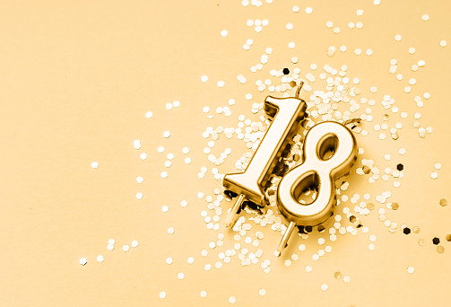 18 years birthday celebration festive background made with golden candle in the form of number Eighteen lying on sparkles. Universal holiday banner with copy space.