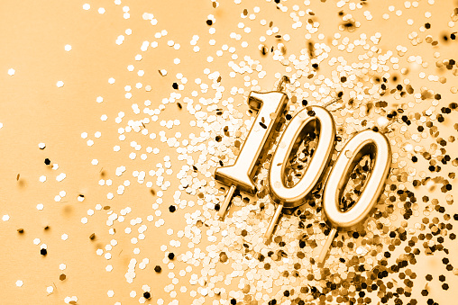 100 years celebration festive background made with golden candles in the form of number Hundred lying on sparkles. Universal holiday banner with copy space.