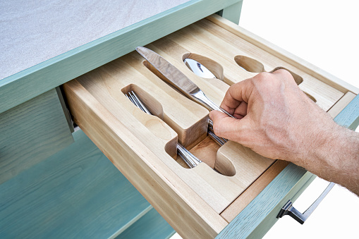 Man hand puts knife in craved wooden holder in kitchen cabinet drawer closeup. Person takes cutlery from storage tray. Home furniture