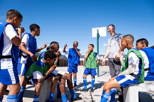 A team of soccer players and their coach enjoy healthy oranges for their half time snack during their friendly game amongst themselves. Soccer practice at a rural school near Cape Town, South Africa