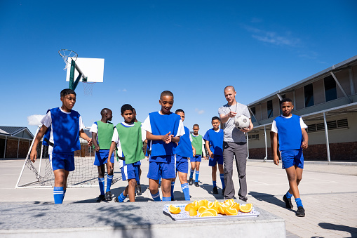 A team of soccer players and their coach enjoy healthy oranges for their half time snack during their friendly game amongst themselves. Soccer practice at a rural school near Cape Town, South Africa