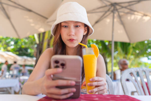 istock Gen Z Asian Woman Enjoying Ice Blended Mango Fruit Punch at Beachside Restaurant While Using Smartphone 1798085302