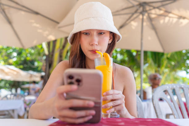 istock Gen Z Asian Woman Enjoying Ice Blended Mango Fruit Punch at Beachside Restaurant While Using Smartphone 1798085825