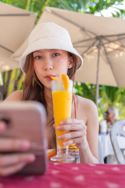 istock Gen Z Asian Woman Enjoying Ice Blended Mango Fruit Punch at Beachside Restaurant While Using Smartphone 1798086341